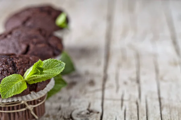 Muffins escuros de chocolate com folhas de hortelã closeup em madeira rústica — Fotografia de Stock
