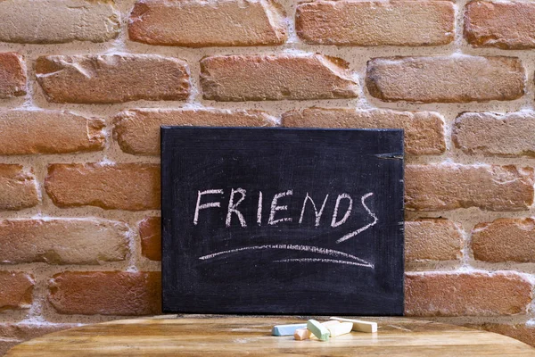 Svart tavla med ordet vänner drunkna för hand på träbord — Stockfoto