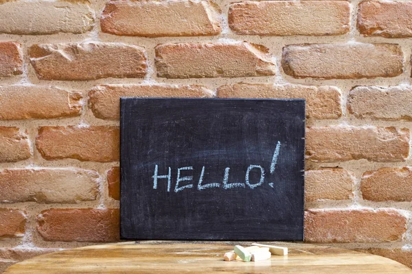 Placa preta com a palavra HELLO! afogar à mão na mesa de madeira o — Fotografia de Stock