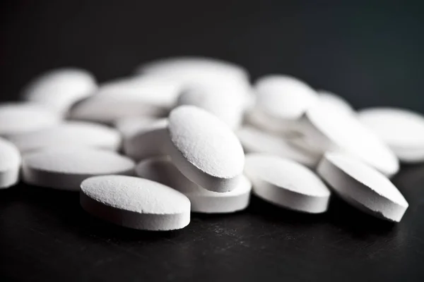 Pilha de pílulas de drogas brancas que colocam no fundo da placa preta . — Fotografia de Stock