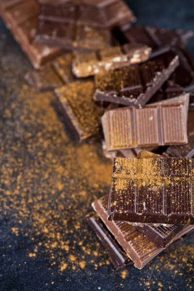 Broken chocolate stacked on black background. Chocolate bar piec — Stock Photo, Image