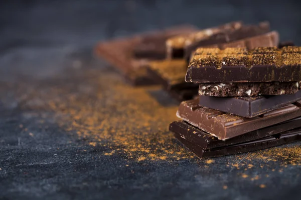 Gebroken chocolade gestapeld op zwarte achtergrond. Chocoladereep Piec — Stockfoto