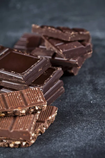 Brocken gebrochener Schokolade auf schwarzem Brett gestapelt. — Stockfoto