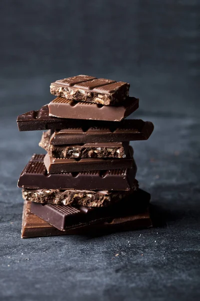 Chunks of broken chocolate stacked on black board. — Stock Photo, Image