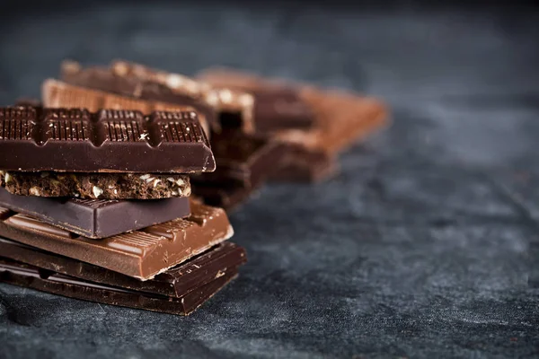 깨진 초콜릿 덩어리가 검은 색 보드에 쌓여 있습니다. 초콜릿 바 — 스톡 사진
