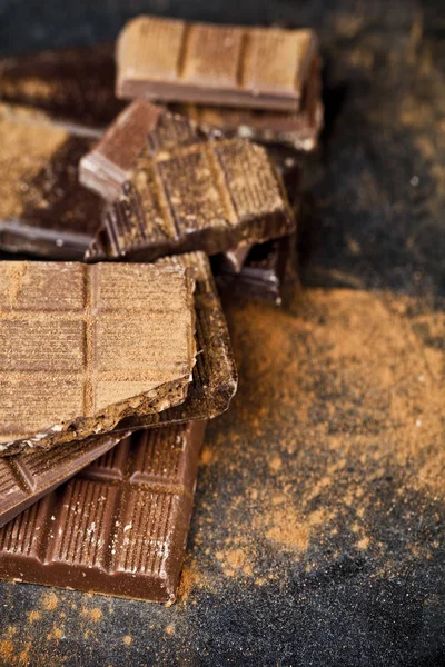 Broken chocolate stacked on black background. Chocolate bar piec — Stock Photo, Image
