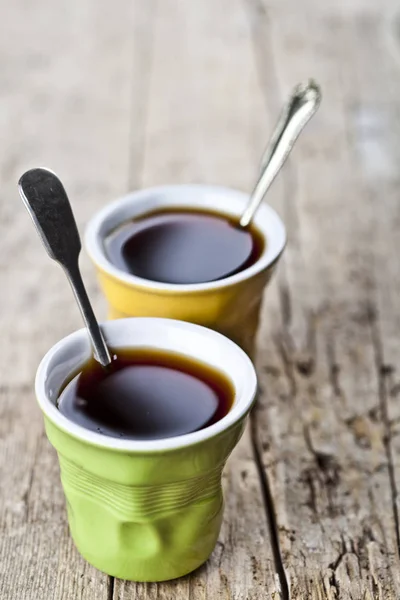 Green and yellow cups with black coffe and spoons on rustic wood — Stock Photo, Image