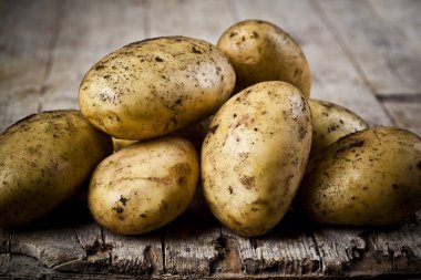 Rustik ahşap arka plan üzerinde yeni hasat kirli patates yığını.