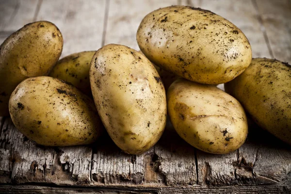 Newly harvested dirty potatoes heap on rustic wooden background. — Stock Photo, Image
