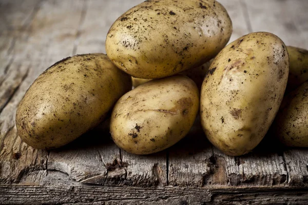 Papas sucias recién cosechadas amontonadas sobre fondo rústico de madera . — Foto de Stock