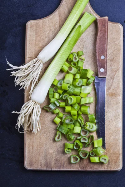 Φρέσκα πράσινα βιολογικά κομμένα κρεμμύδια και μαχαίρι σε μια σανίδα κοπής. — Φωτογραφία Αρχείου