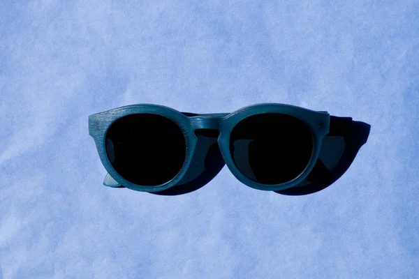 Stylish sunglasses with shadow on blue background. — Stock Photo, Image