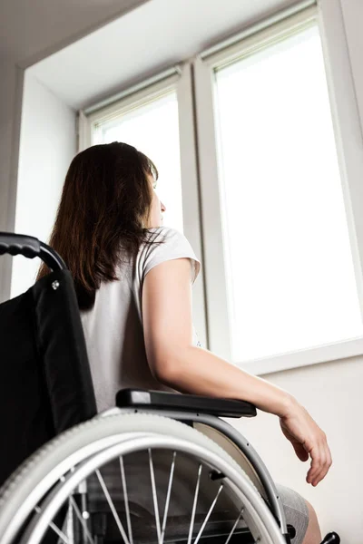 Некоректна або інвалідна жінка сидить на інвалідному кріслі, дивлячись у вікно денного світла — стокове фото