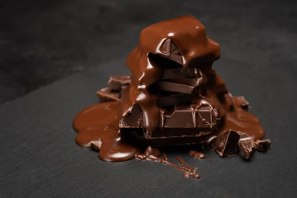 Close up of chocolate pieces pile or heap and melted chocolate syrup on dark concrete background — Stock Photo, Image
