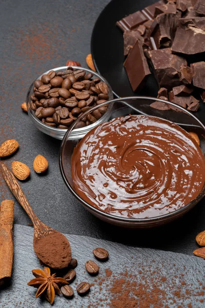 溶けたチョコレートやヘーゼルナッツは、暗いコンクリートの背景にガラスボウルとチョコレートの部分に広がります — ストック写真