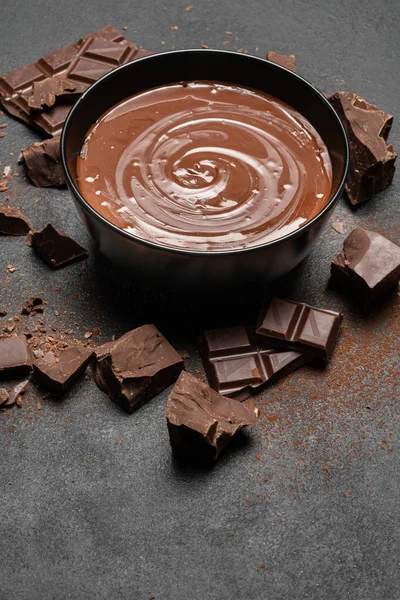 Keramische kom van chocolade crème of gesmolten chocolade en stukjes chocolade geïsoleerd op donkere betonnen achtergrond — Stockfoto