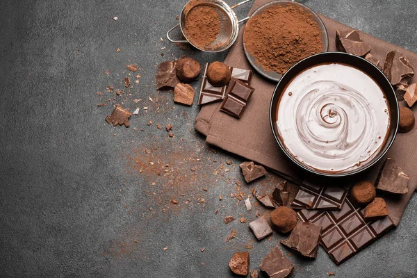 ceramic bowl of chocolate cream or melted chocolate and pieces of chocolate isolated on dark concrete background