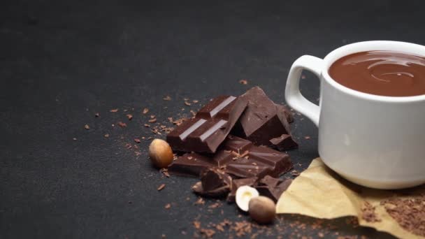 Cup of hot chocolate and pieces of chocolate on dark concrete background — Stock Video