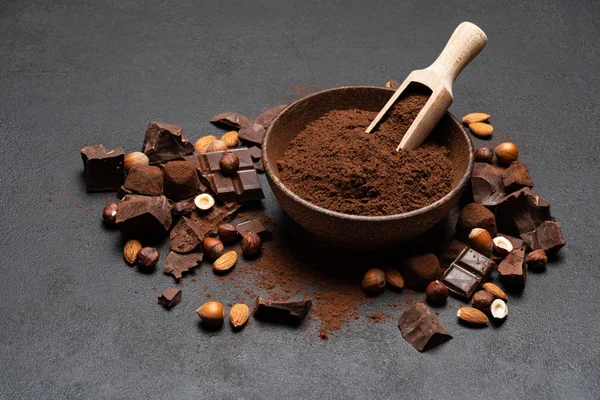 Dark Chocolate chunks, nuts and cocoa powder in wooden bowl on dark concrete background