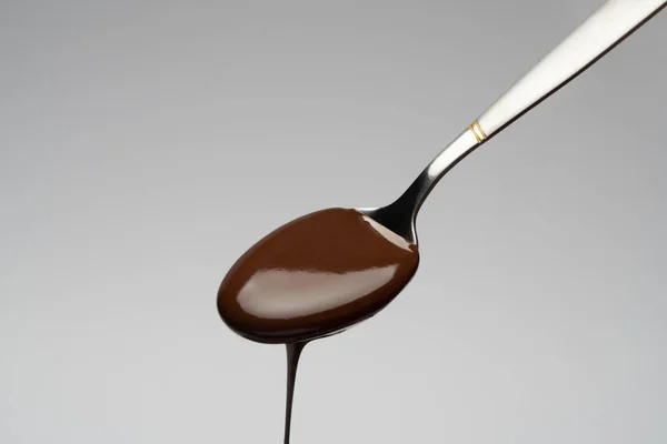 Cioccolato liquido su un cucchiaio su fondo grigio chiaro — Foto Stock