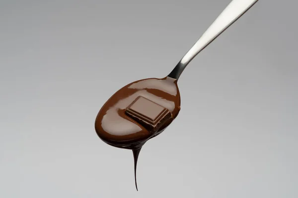 Cioccolato liquido su un cucchiaio su fondo grigio chiaro — Foto Stock