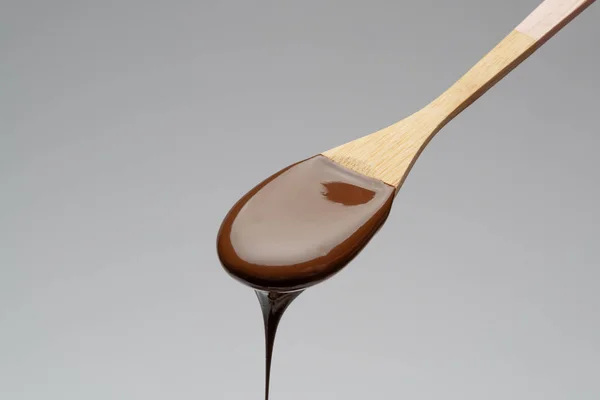 Cioccolato liquido su un cucchiaio di legno su fondo grigio chiaro — Foto Stock