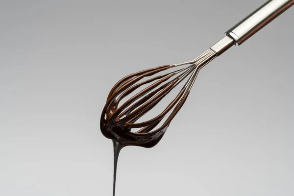 Whisk z ciekłą roztopioną czekoladą na jasnoszarym tle — Zdjęcie stockowe