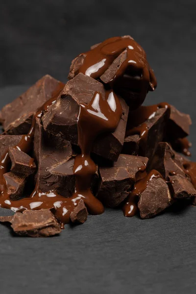 Dunkle oder milchige Schokoladenstücke stapeln sich und Schokoladensirup auf dunklem Betongrund — Stockfoto
