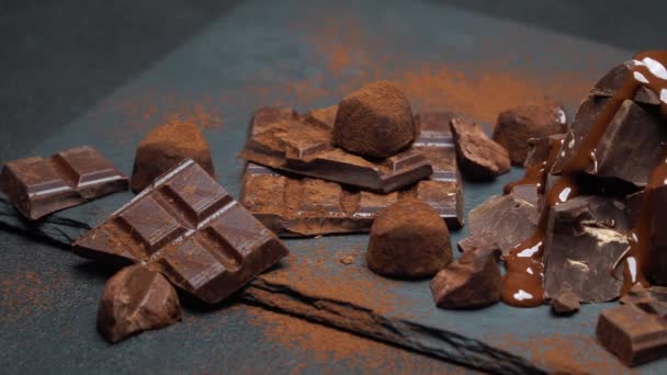 Dark or milk chocolate pieces, chocolate syrup and truffle candies on dark concrete background — Stock Video