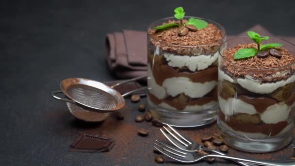 Zwei Portionen klassisches Tiramisu-Dessert in Glas und Schokoriegel auf dunklem Betongrund — Stockvideo