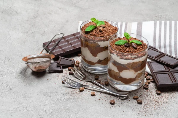 Due porzioni Classico dessert tiramisù in un bicchiere e tavoletta di cioccolato su sfondo di cemento — Foto Stock