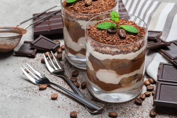 Due porzioni Classico dessert tiramisù in un bicchiere e tavoletta di cioccolato su sfondo di cemento — Foto Stock