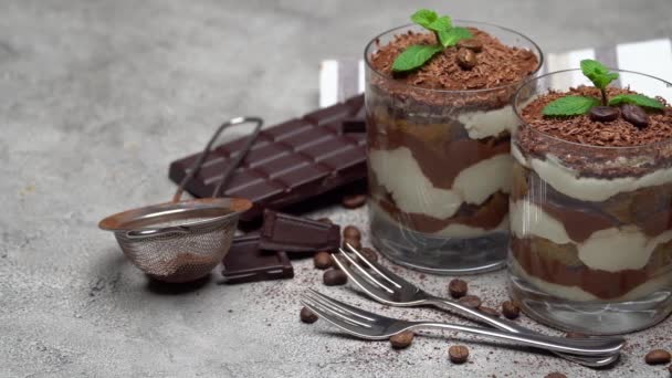 Two portions Classic tiramisu dessert in a glass and chocolate bar on concrete background — Stock Video