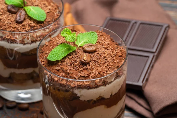 Zwei Portionen klassisches Tiramisu-Dessert in Glas und Schokoriegel auf Holzgrund — Stockfoto