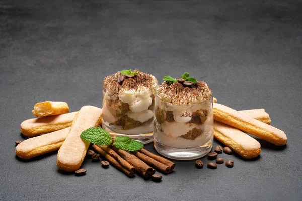 Dessert tiramisù classico in bicchiere e biscotti savoiardi su fondo di cemento scuro — Foto Stock