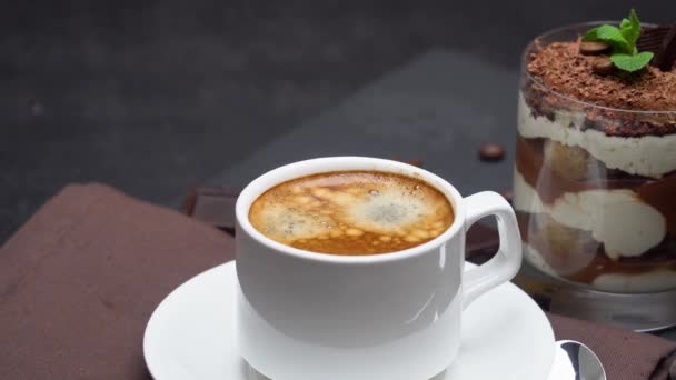Postre tiramisú clásico en un vaso y una taza de café sobre fondo de hormigón oscuro — Vídeos de Stock