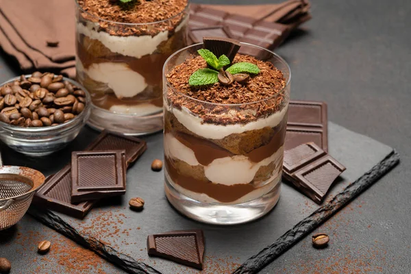 Classico dessert tiramisù in un bicchiere e pezzi di cioccolato su sfondo di cemento scuro — Foto Stock