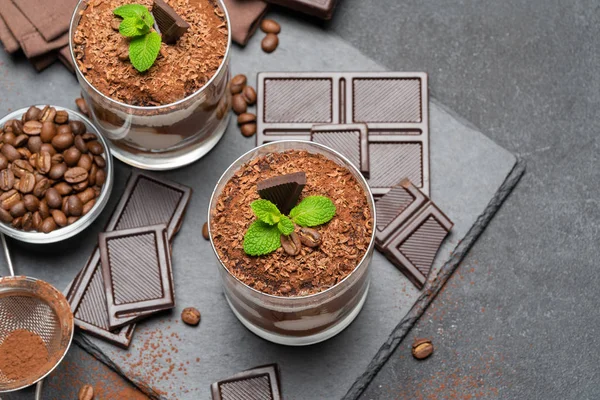 Klassisches Tiramisu-Dessert im Glas und Schokoladenstücke auf dunklem Betongrund — Stockfoto