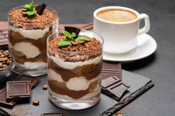 Classico dessert tiramisù in un bicchiere e una tazza di caffè su sfondo di cemento scuro — Foto Stock