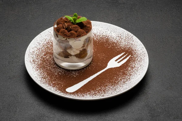 Классический десерт тирамису в стакане на тарелке с силуэтом вилки на темно-бетонном фоне — стоковое фото