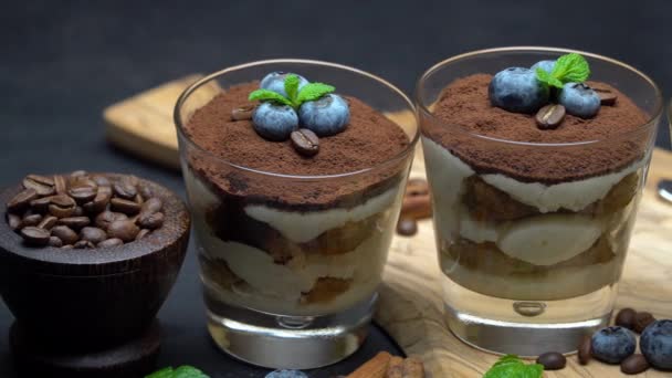 Класичний десерт тірамісу в келиху з чорницею на темному бетонному фоні — стокове відео