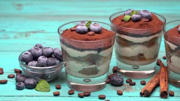 Dessert classique au tiramisu dans un verre aux myrtilles sur fond de bois bleu — Video
