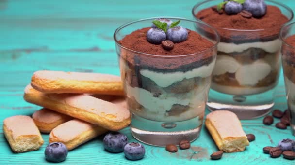 Dessert tiramisù classico in un bicchiere con mirtilli su fondo di legno blu — Video Stock