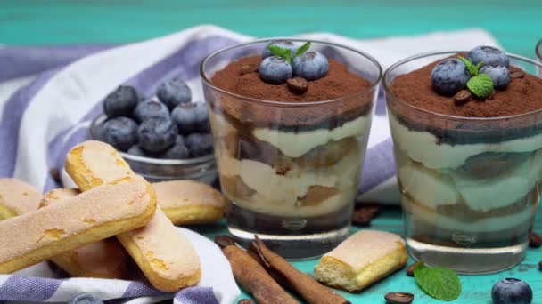 Klassisches Tiramisu-Dessert im Glas mit Blaubeeren auf blauem Holzgrund — Stockvideo