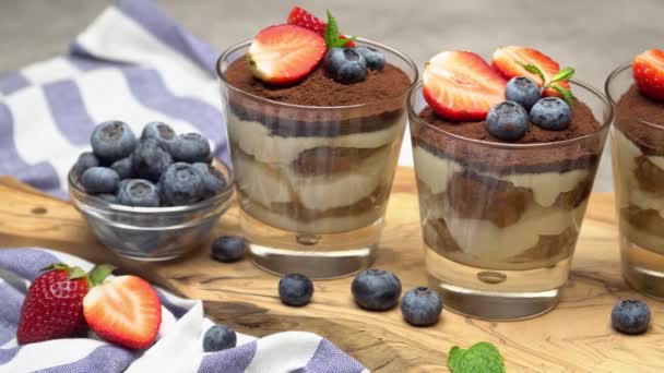 经典的提拉米苏甜点，在混凝土背景的玻璃杯中搭配蓝莓和草莓 — 图库视频影像