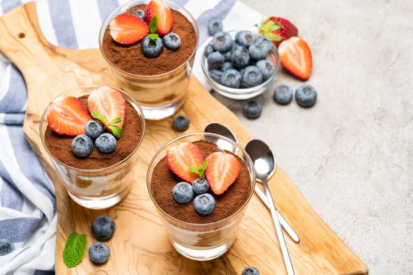 Sobremesa tiramisu clássica com mirtilos e morangos em um copo no fundo de concreto — Fotografia de Stock