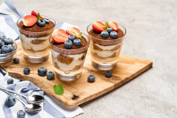 Klassisches Tiramisu-Dessert mit Blaubeeren und Erdbeeren im Glas auf Betongrund — Stockfoto