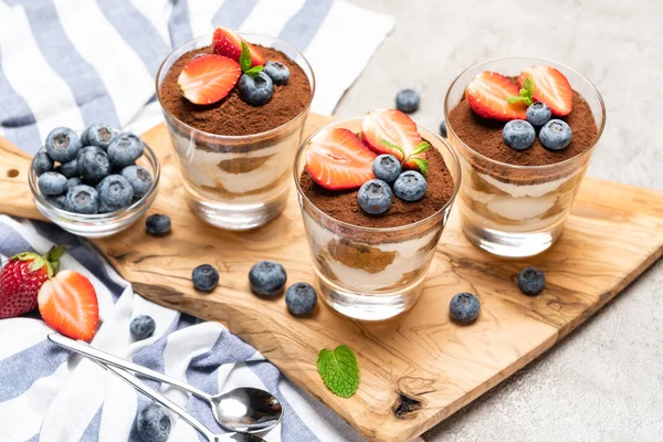 Sobremesa tiramisu clássica com mirtilos e morangos em um copo no fundo de concreto — Fotografia de Stock