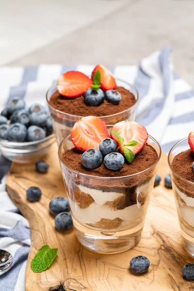 Classic tiramisu dessert with blueberries and strawberries in a glass on concrete background — Stock Photo, Image