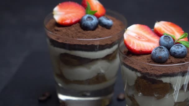 Klassisches Tiramisu-Dessert mit Blaubeeren und Erdbeeren im Glas auf dunklem Betongrund — Stockvideo